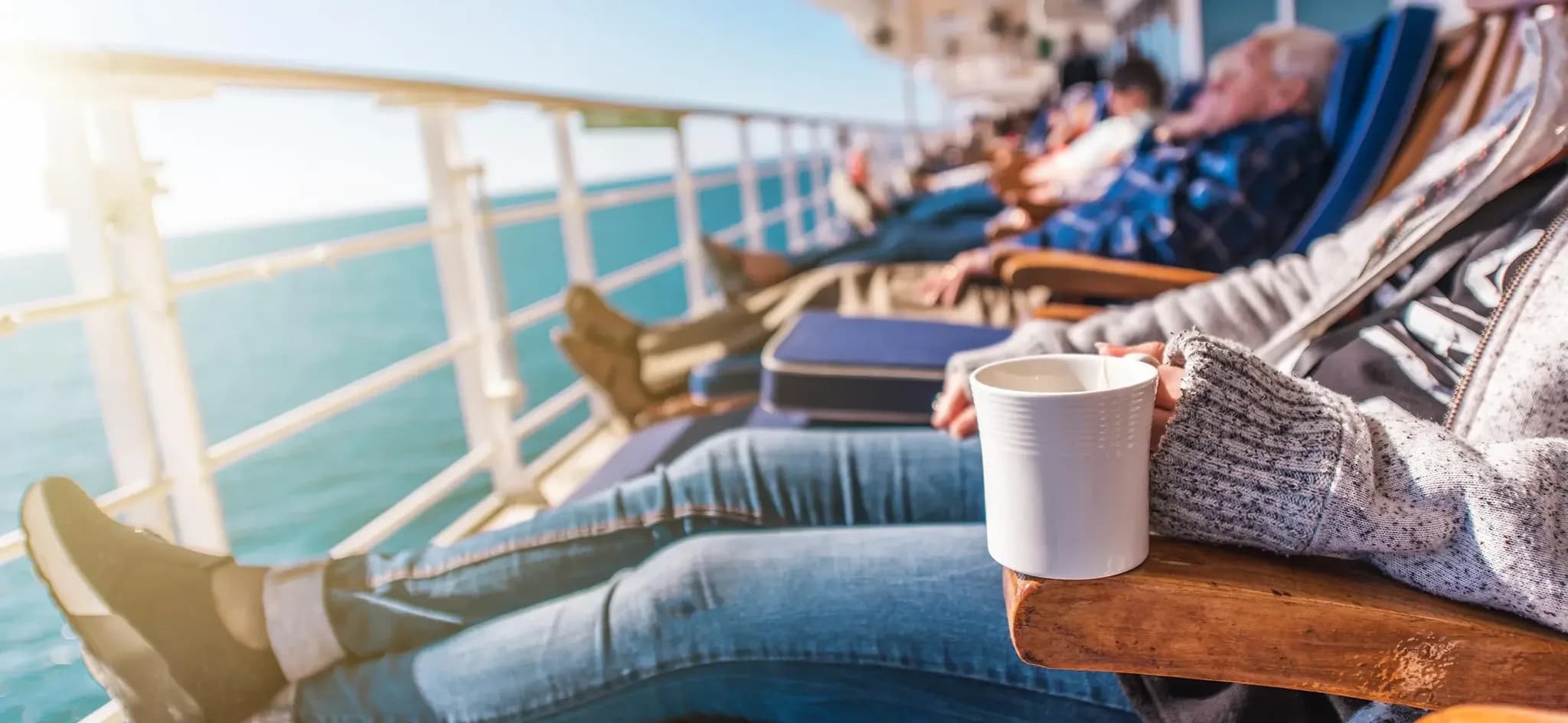Menschen entspannen in Liegestühlen an Deck eines Kreuzfahrtschiffs mit Blick aufs Meer